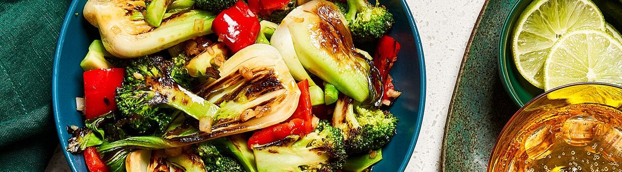 Charred bok choy and broccoli in a blue bowl on a white countertop.