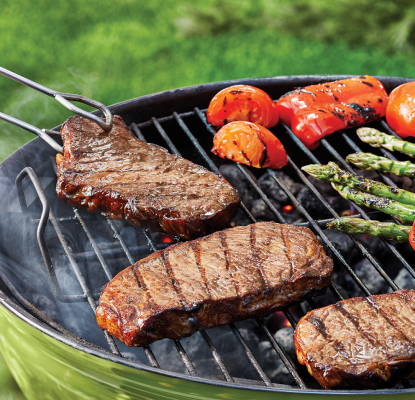 Steaks on a bbq grill, sizzling alongside red pepeprs and asparagus.