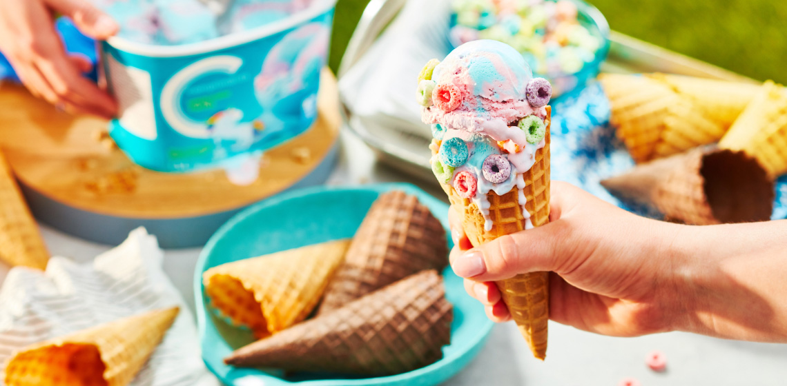 Hand holding waffle ice cream cone with unicorn twirl ice cream scoops