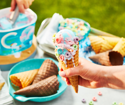 Hand holding waffle ice cream cone with unicorn twirl ice cream scoops