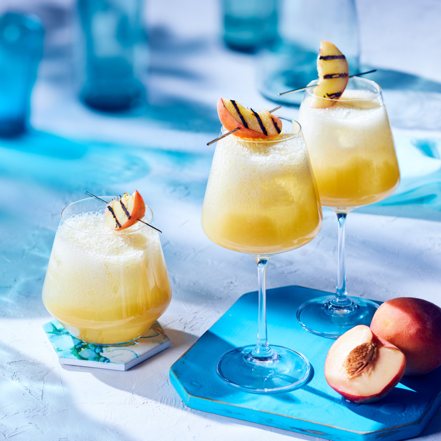three wine glasses of peach-bourbon cocktail with grilled peach slice garnish