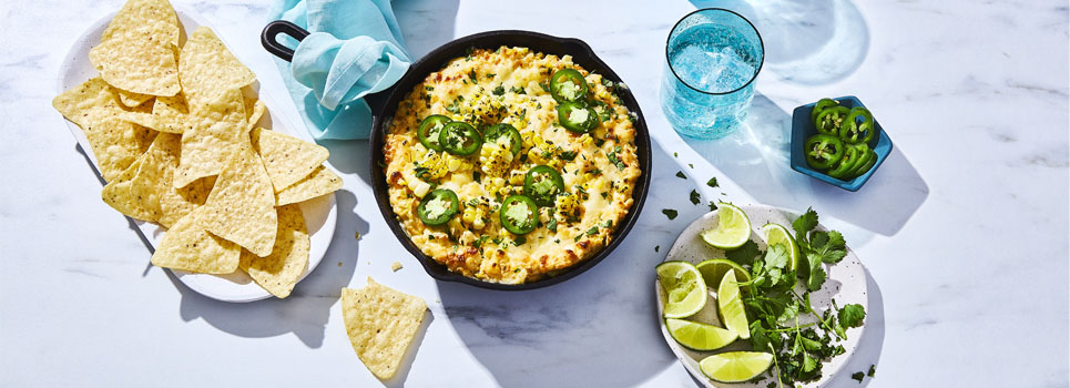 cast-iron pan of Mexican-inspired Street Corn Party Dip with tortilla chips on the side