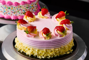 Strawberry Lemonade Cake on cake stand, with confetti cake in background being decorated