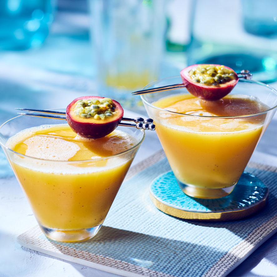 two short v-shaped glasses with a yellow passionfruit cocktail and passionfruit garnish on the rim