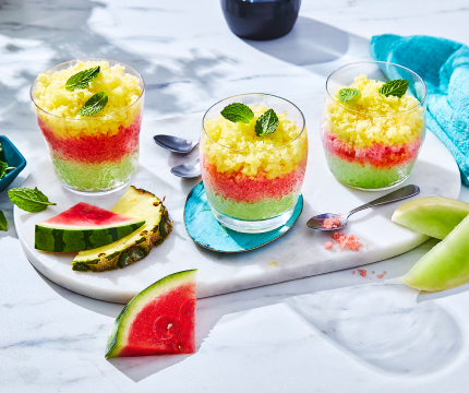 Three lowball glasses of frozen layered melon granita on a serving board with slices of melon in the foreground