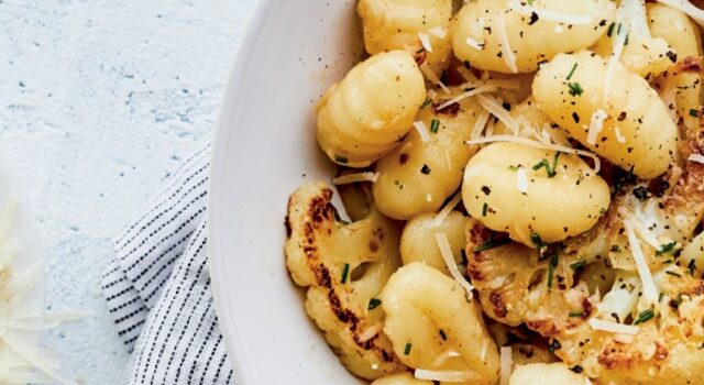 Large white serving bowl filled with gnocchi and roasted cauliflower on marble tabletop