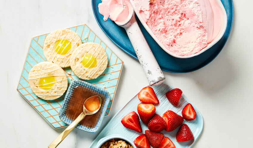 Strawberry lemon shortcake sundae in a tall glass featuring lemon sugar cookies, strawberry shortcake ice cream, fresh strawberries topped with fresh fruit and a strawberry topping.