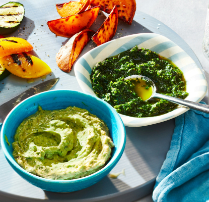 Two bowls of fresh summer herb sauces with grilled vegetables in background